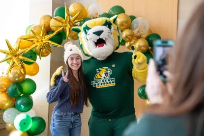 Student making a peace sign with their hands while standing next to Wildcat Willy for a photo op.