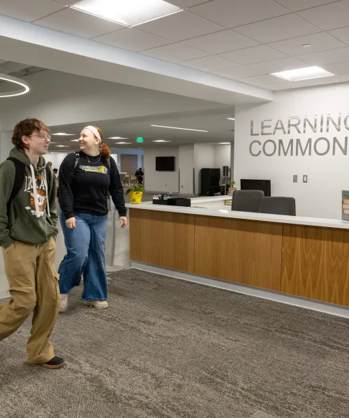 Picture of three students walking past the Learning Commons desk in the Olson library while smiling
